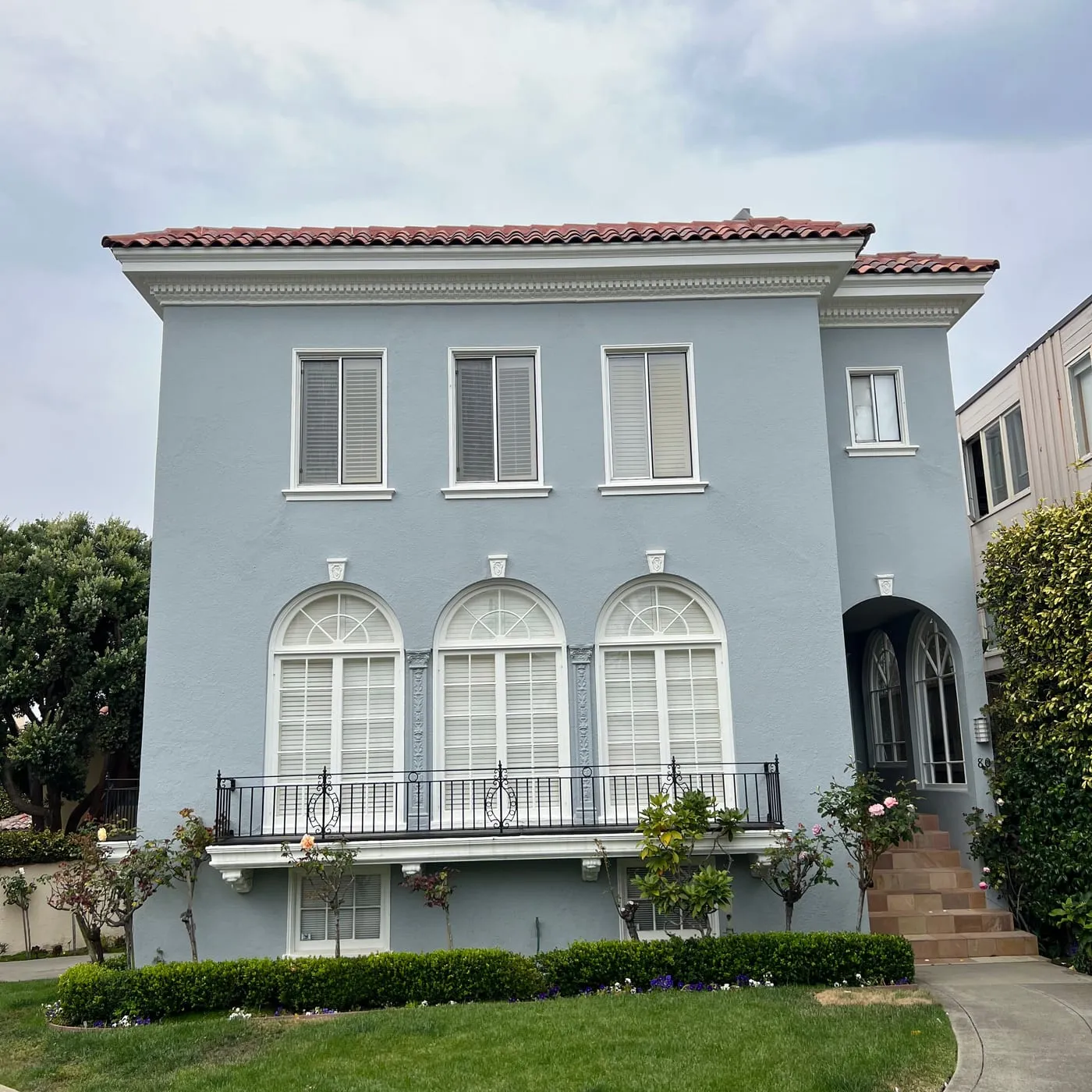 Blue-grey San Francisco home with arched windows, tile roofline and an iron balcony rail after repainting